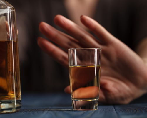 Hand pushing away a glass containing an alcoholic beverage