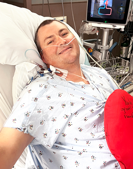 Dan in a hospital bed at UAB St. Vincent's East holding a plush heart stuffed toy. 