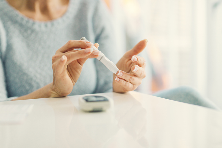 woman taking a blood sugar test on her finger sitting at a table