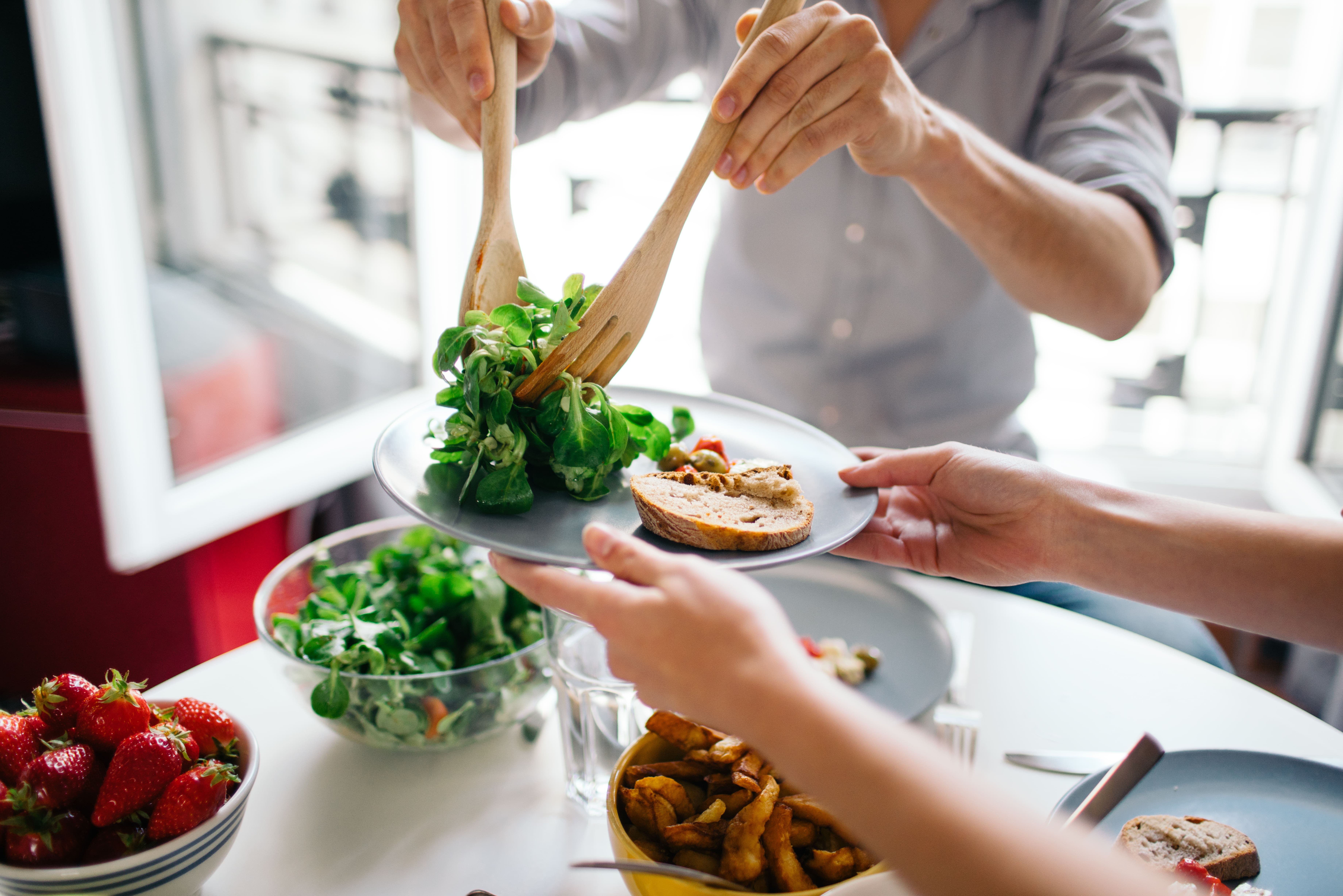 Hands serving a salad to a person holding a plate out. 
