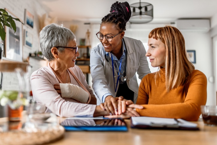 Senior woman and middle-aged woman sitting while consulting with a doctor at a home visit.
