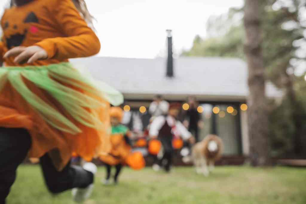 Children dressed in bright Halloween costumes run outside a house with festive decorations, highlighting the importance of visibility and safety while trick-or-treating.