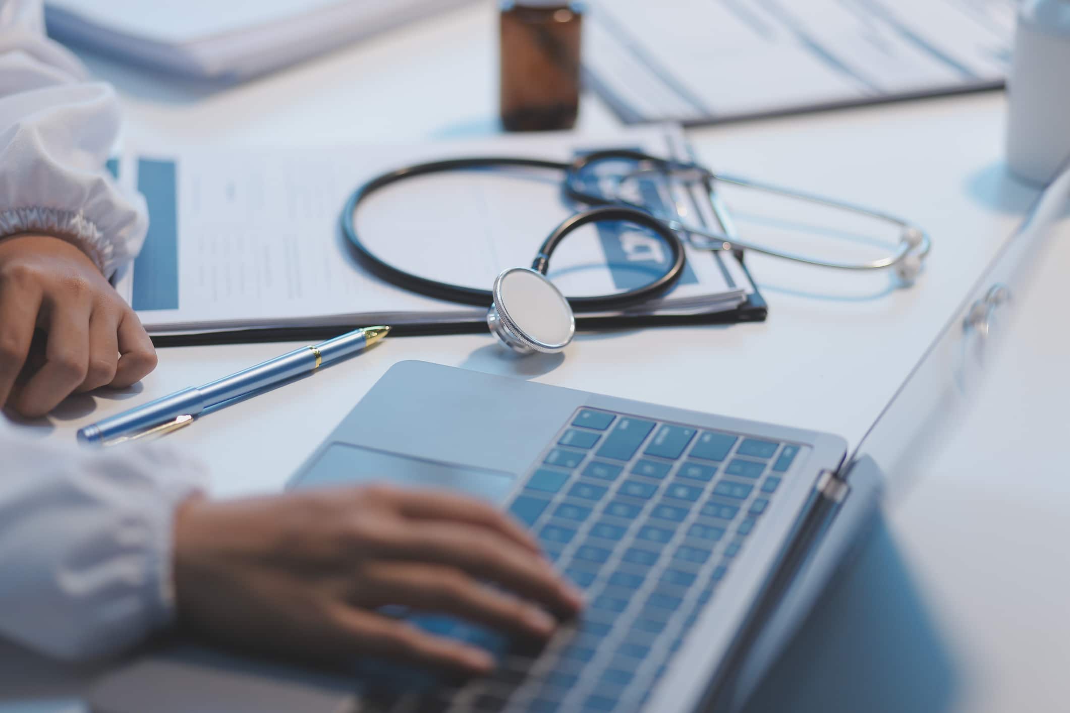 A professional and focused doctor in scrubs is working and reading medical research on her laptop in her office at a hospital.