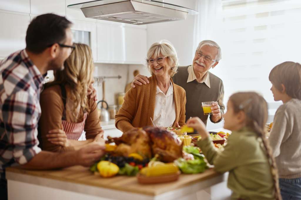 Happy senior grandparents talking to their family while preparing food for Thanksgiving meal in the kitchen.