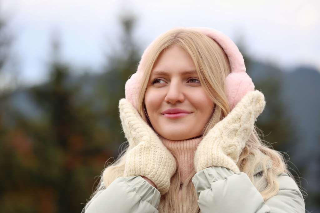 Woman wearing pink earmuffs and knit gloves in cold weather, illustrating how dropping temperatures can affect ear health and cause ear pain or discomfort during winter.