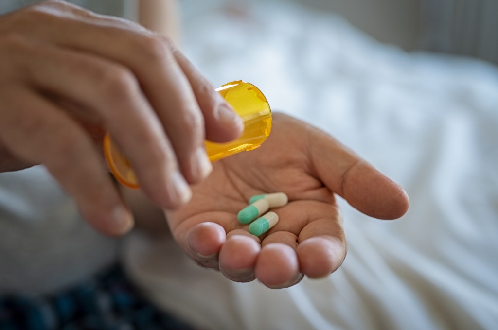Closeup of man hand pouring antibiotic medicine capsules from a pill bottle into hand.