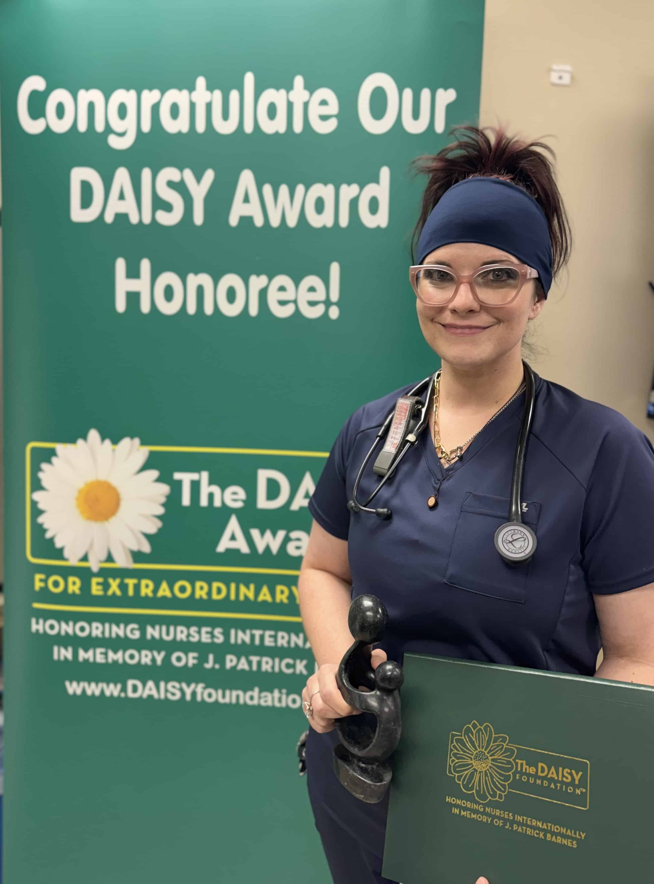 Whitney Humphrey, RN standing with her DAISY award smiling.