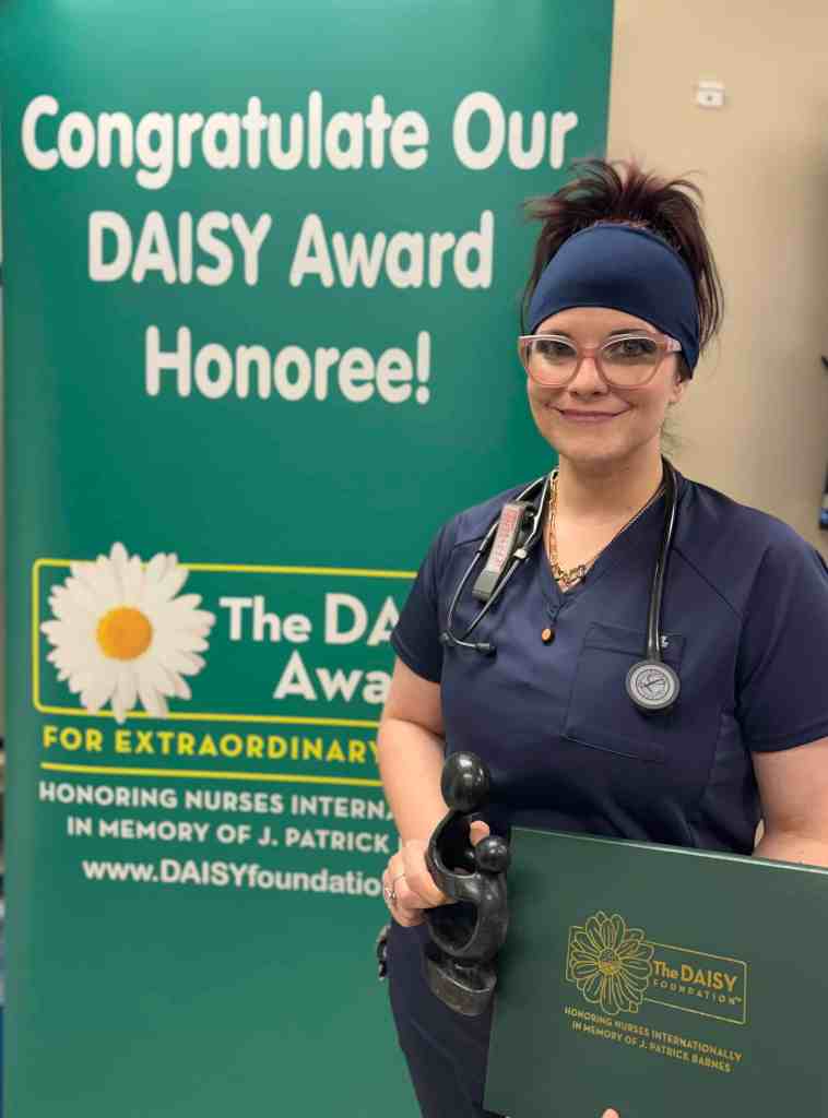 Whitney Humphrey, RN standing with her DAISY Award smiling.