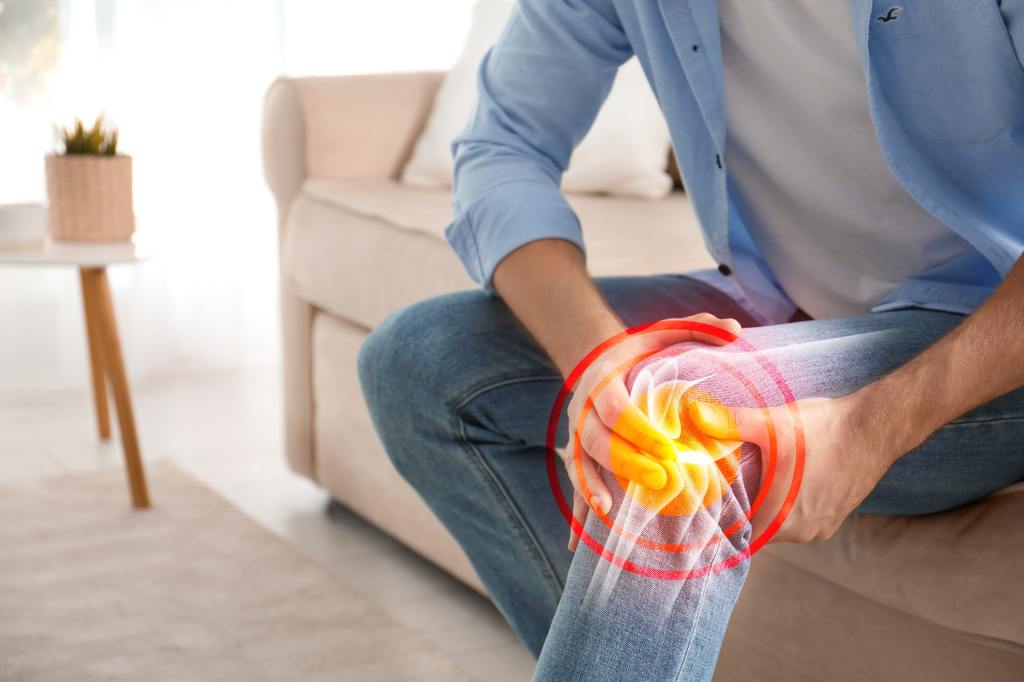 person holds their knee in pain with a virtual rendering of joint pain