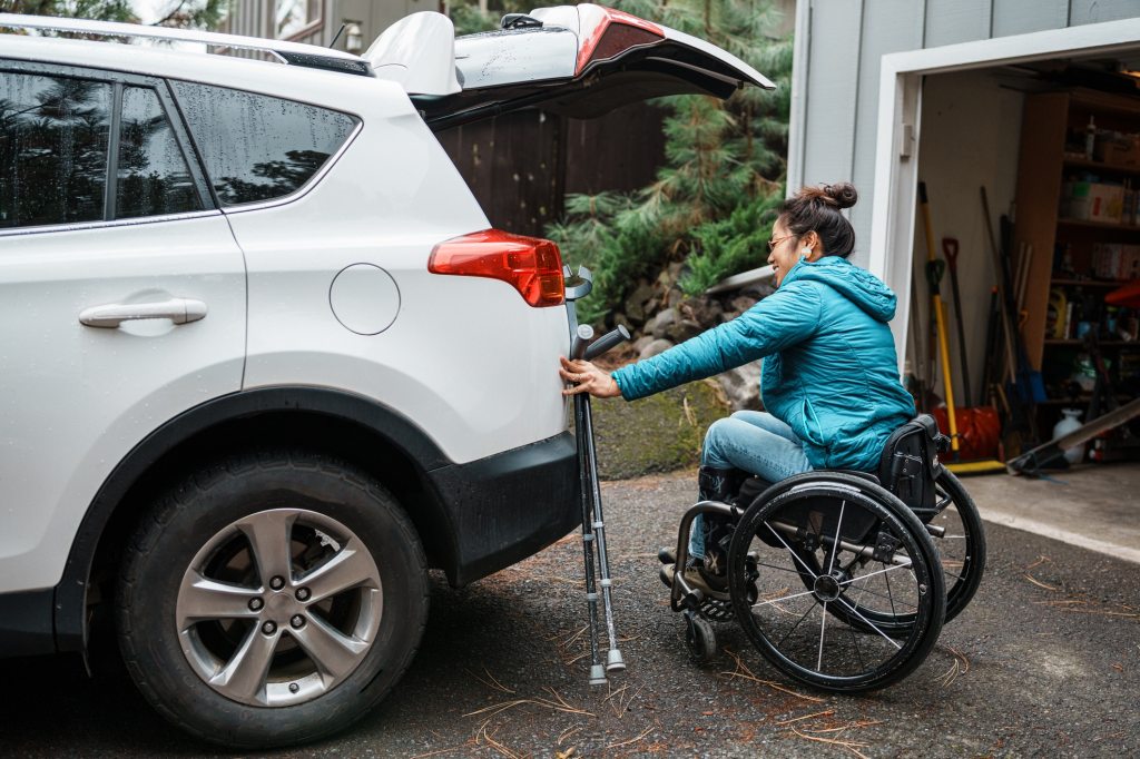 A woman who is using a wheelchair places items in the open trunk of her car