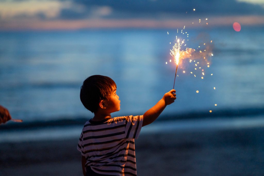 Young boy holding a sparkler firework at dusk