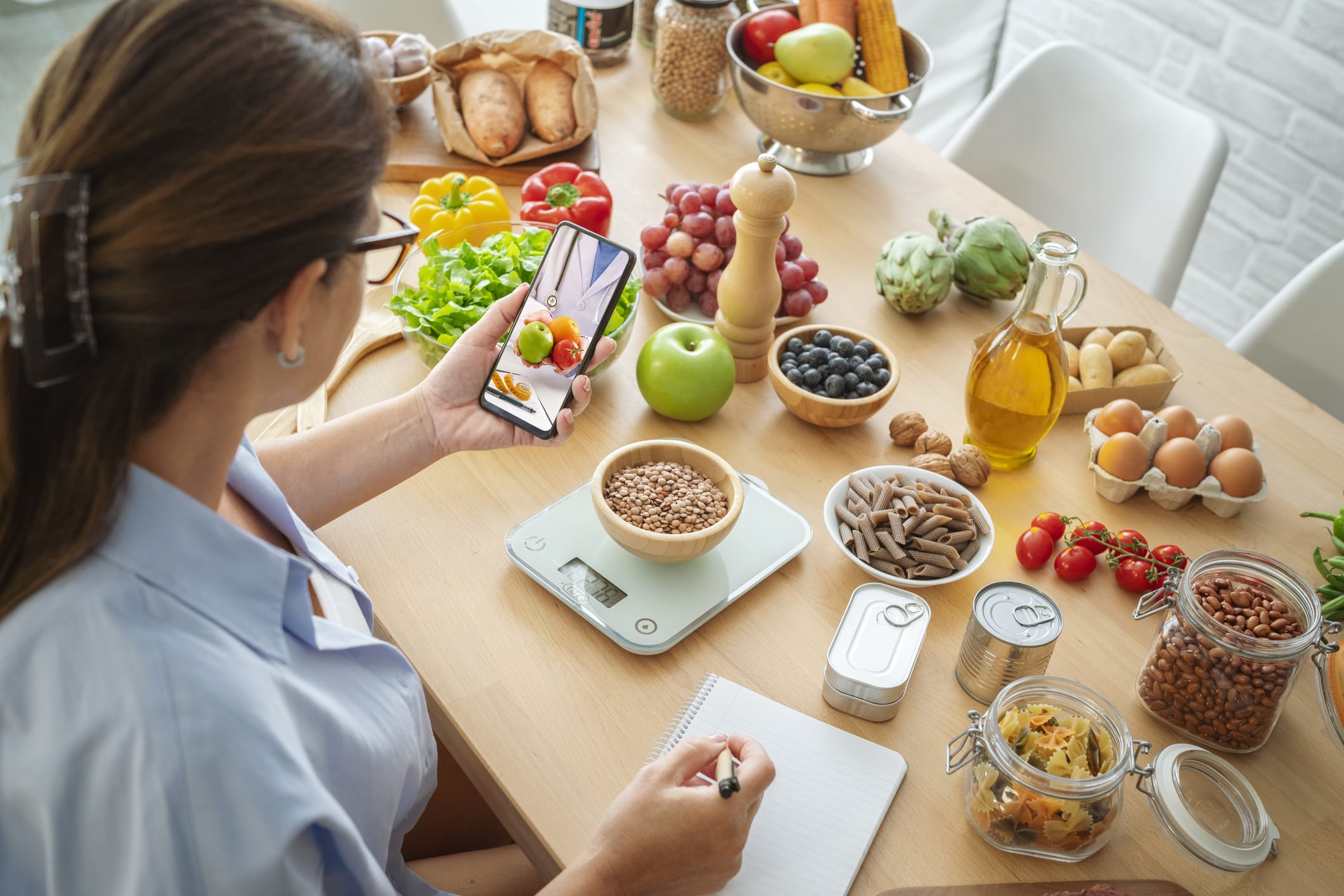 Woman researching recipes on cell phone and taking notes to plan well balanced diet