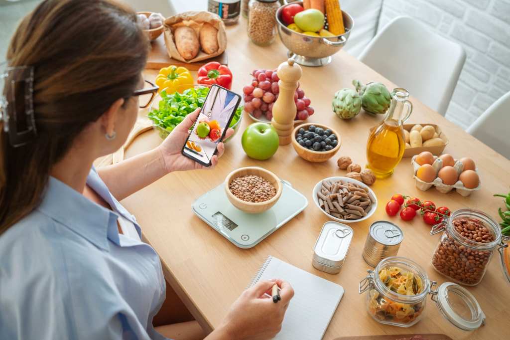 Woman researching recipes on cell phone and taking notes to plan well balanced diet